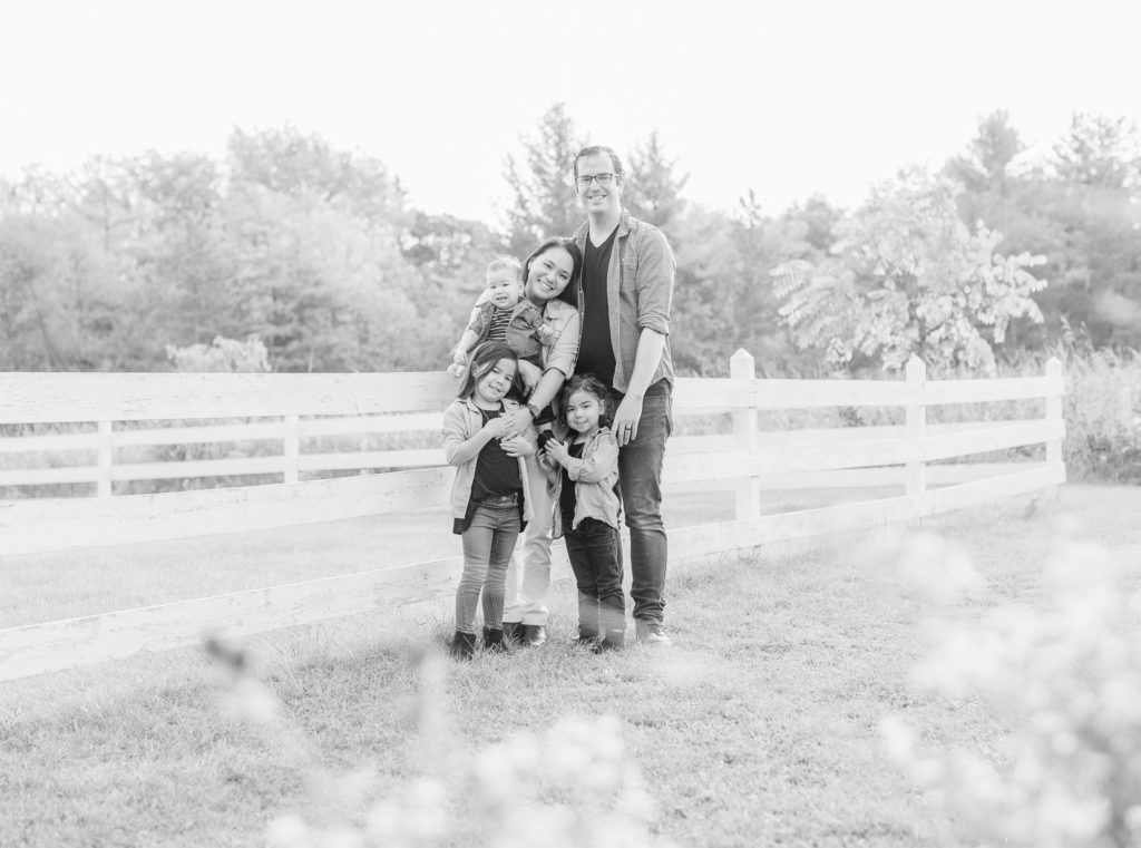 St. Charles, IL. LeRoy Oaks Forest Preserve. Family is standing against a white fence, holding each other, looking at the camera