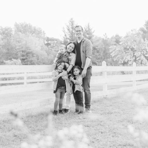 St. Charles, IL. LeRoy Oaks Forest Preserve. Family is standing against a white fence, holding each other, looking at the camera