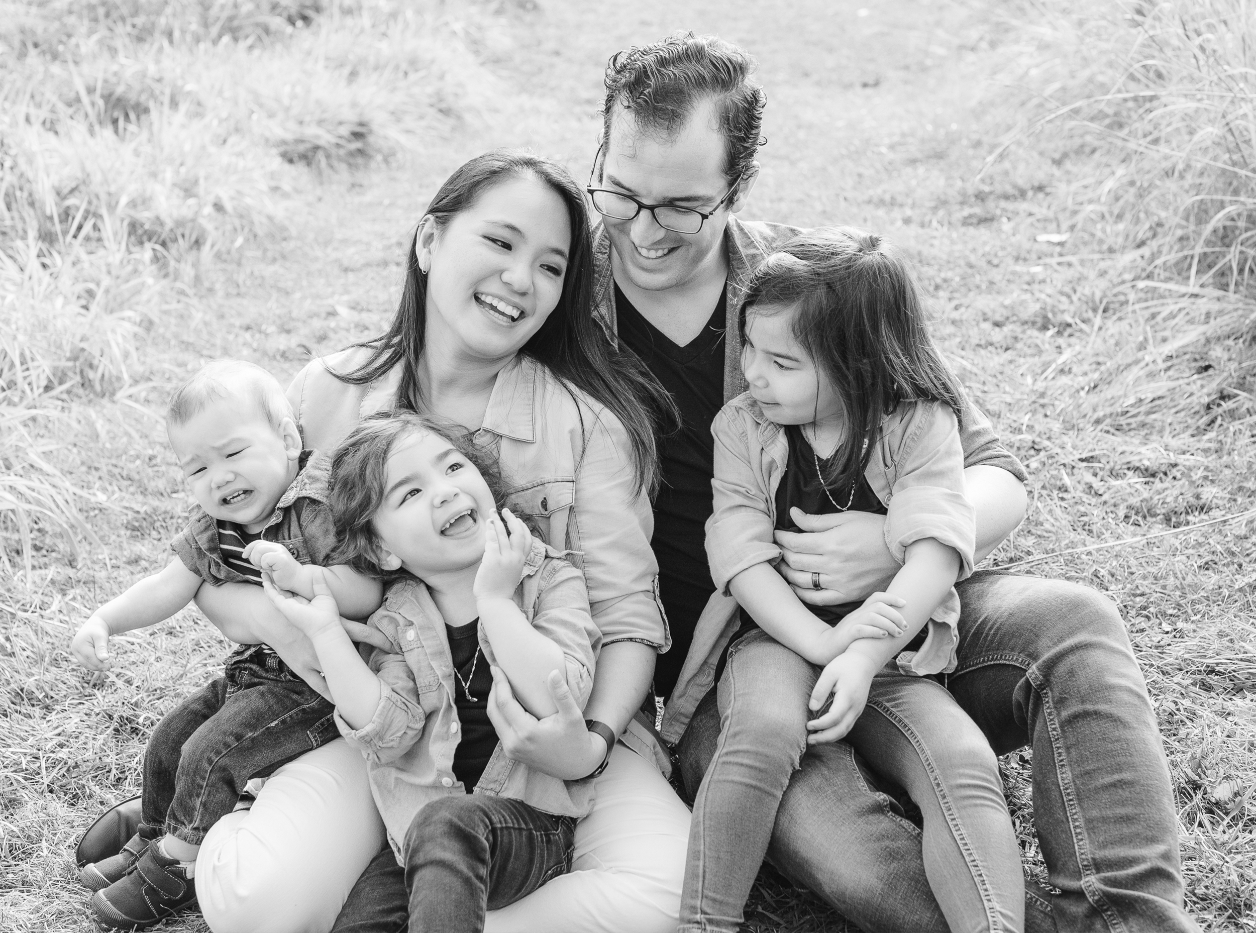 Fall Family Session in St. Charles, IL. LeRoy Oaks Forest Preserve. Family is sitting on the ground. Kids on parent's lap, laughing and looking at each other