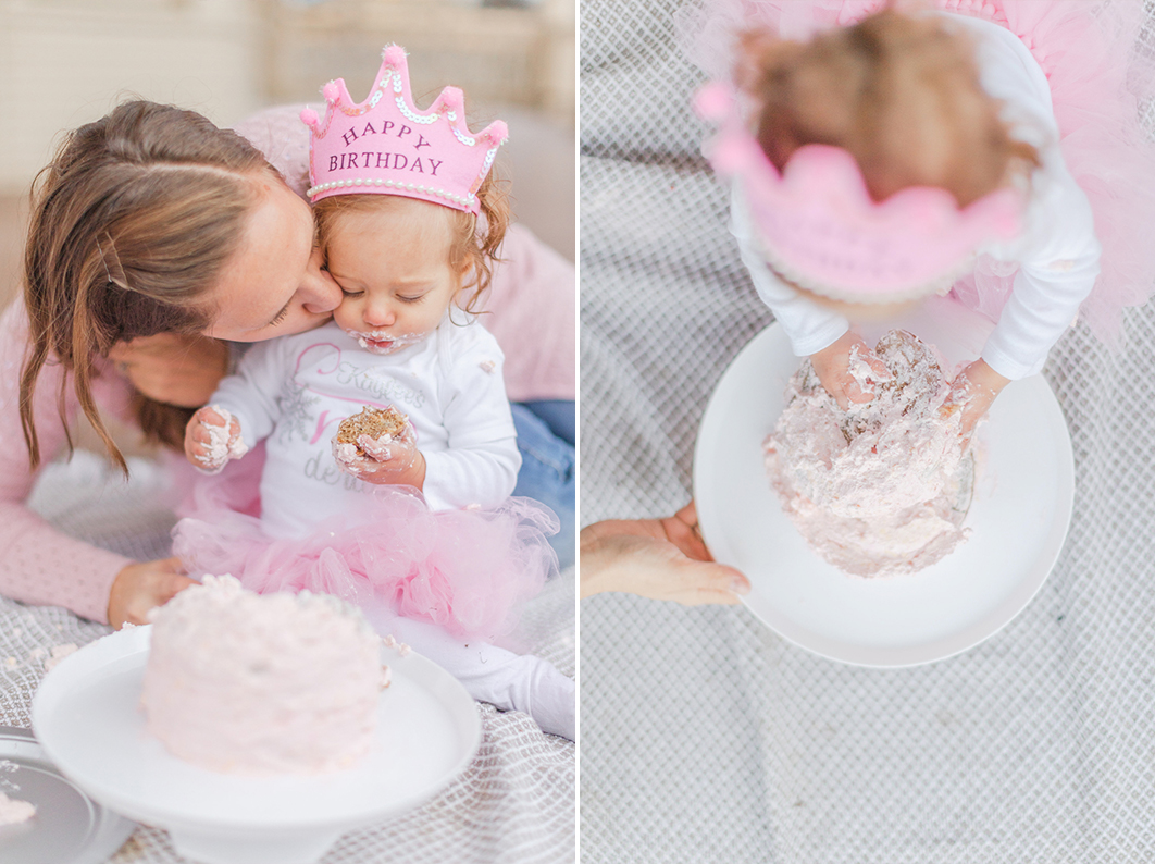 Mom is kissing her one year old on the cheek, while her daughter is eating her first birthday cake