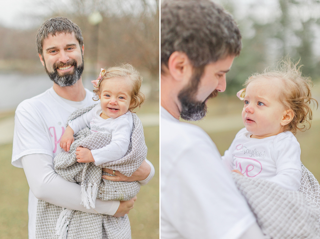 Dad is holding his one year old daughter, smiling into the camera