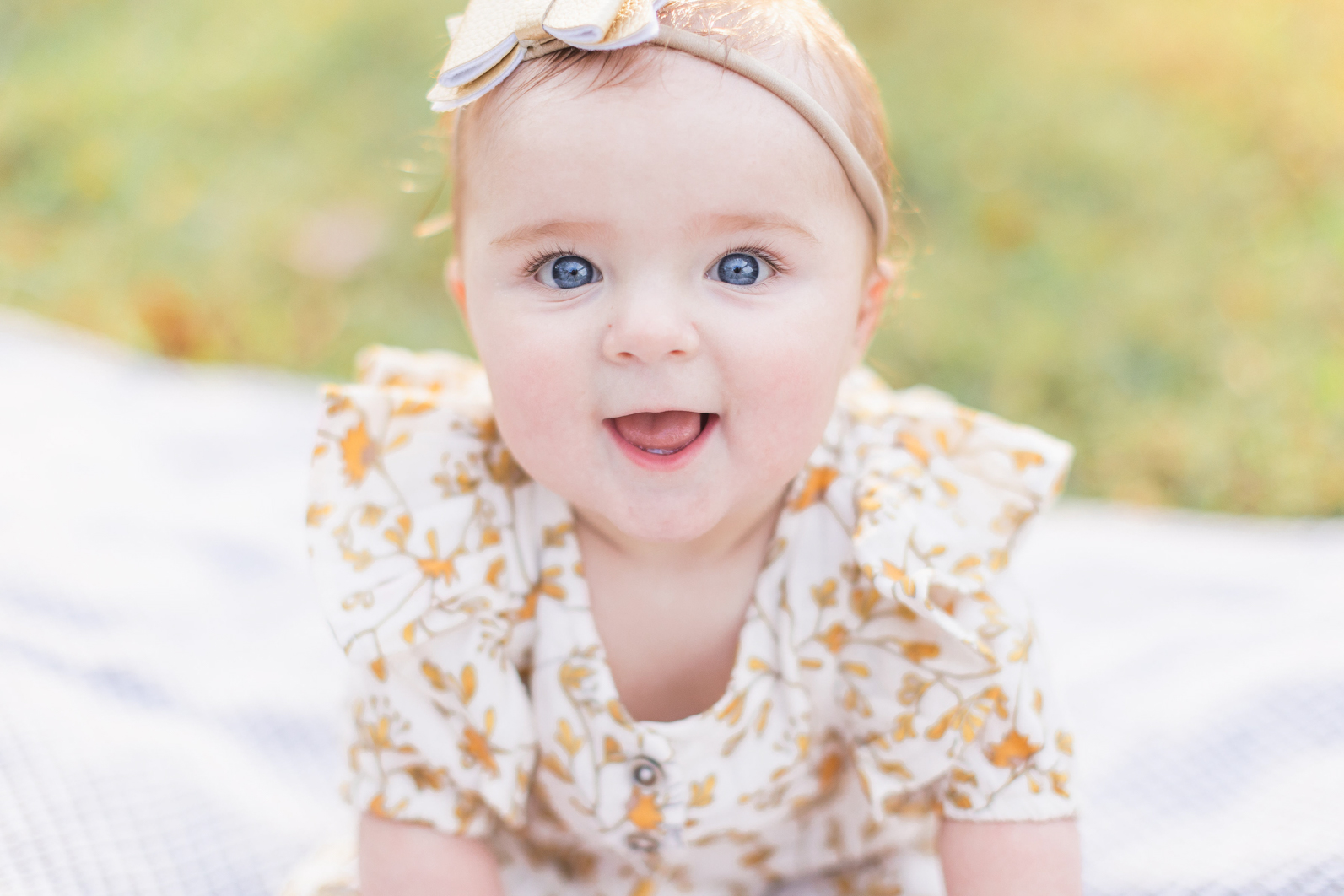 Golden hour mini session McDowell, Charlotte NC. Six month old daughter is sitting on a blanket in the gras laughing into the camera with big blue eyes.