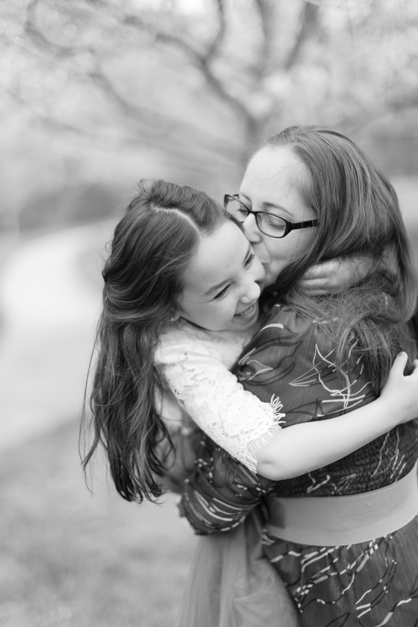 Black and white photo of Mom holding her daughter, giving her a big hug and kissing her on the cheek. Her daughter is smiling big, hugging her back during their charlotte spring minis