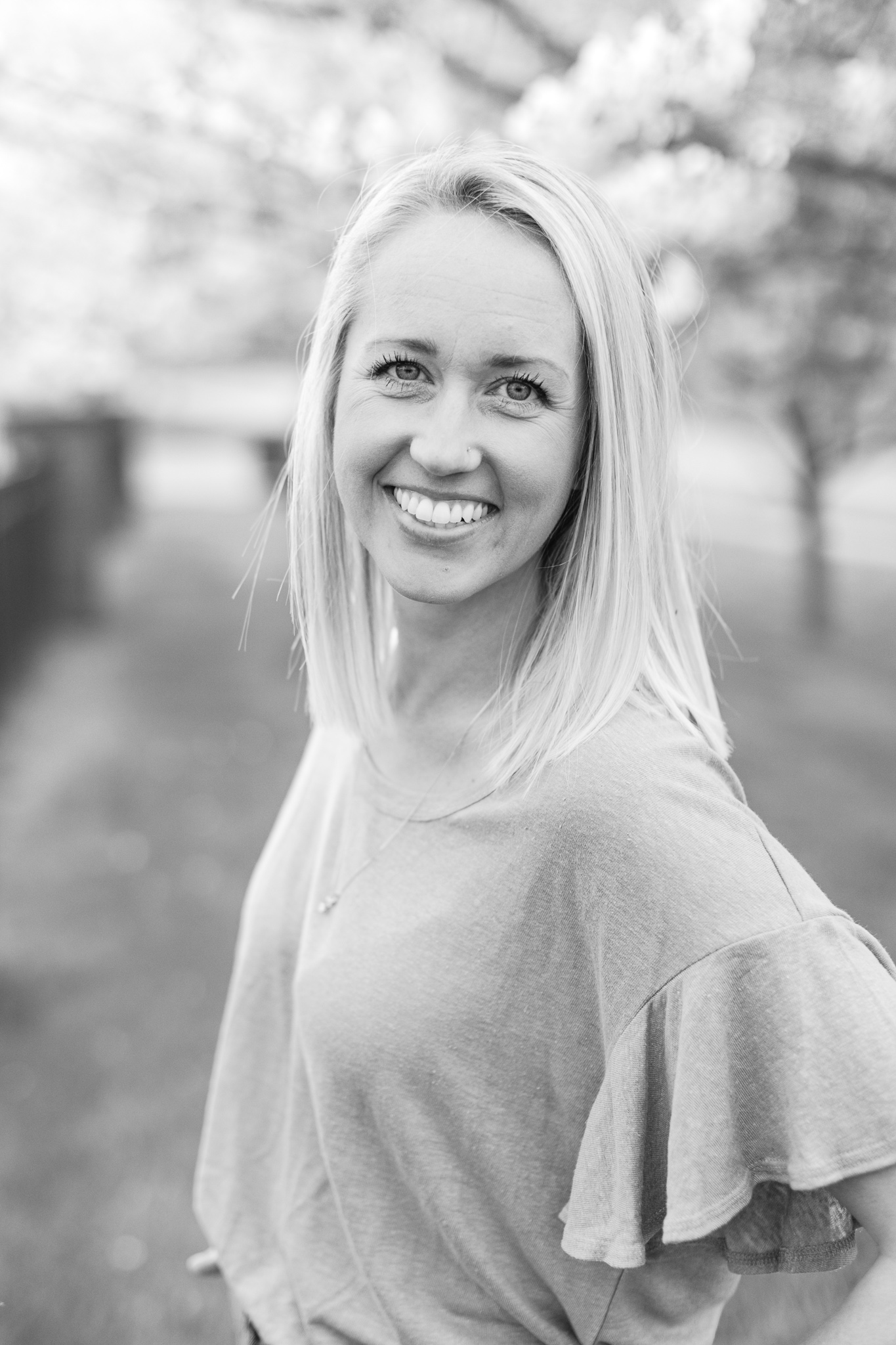 Black and White Portrait of Mom smiling into the camera in front of a white cherry blossom tree.