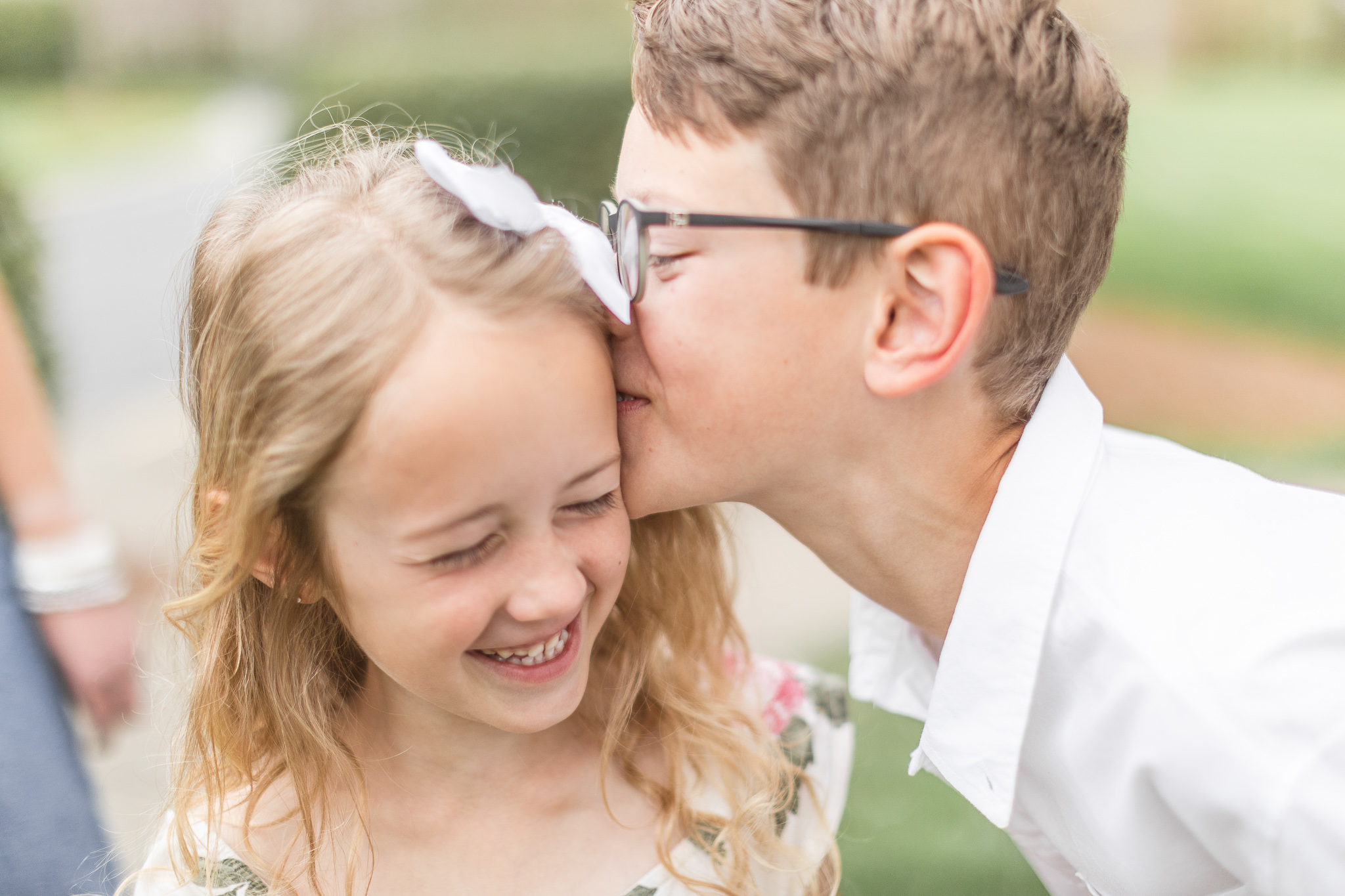 Sister is laughing while brother kisses her on the cheek during a family spring blossom session in Charlotte NC