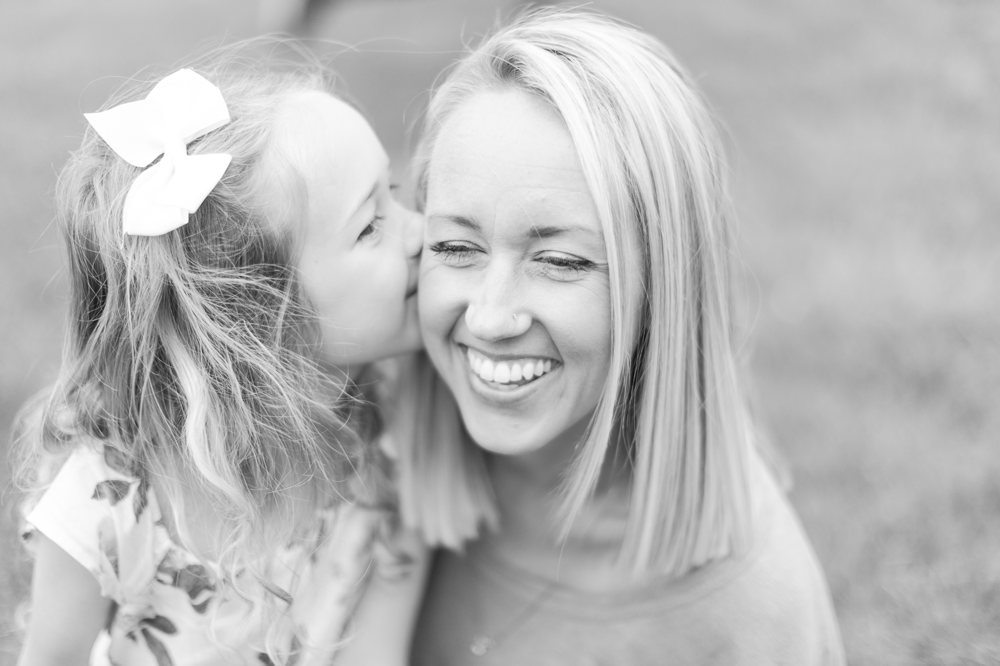 Black and white - Mother is laughing into the distance while her daughter is whispering in her ear during a family spring blossom session in Ballantyne, Charlotte NC