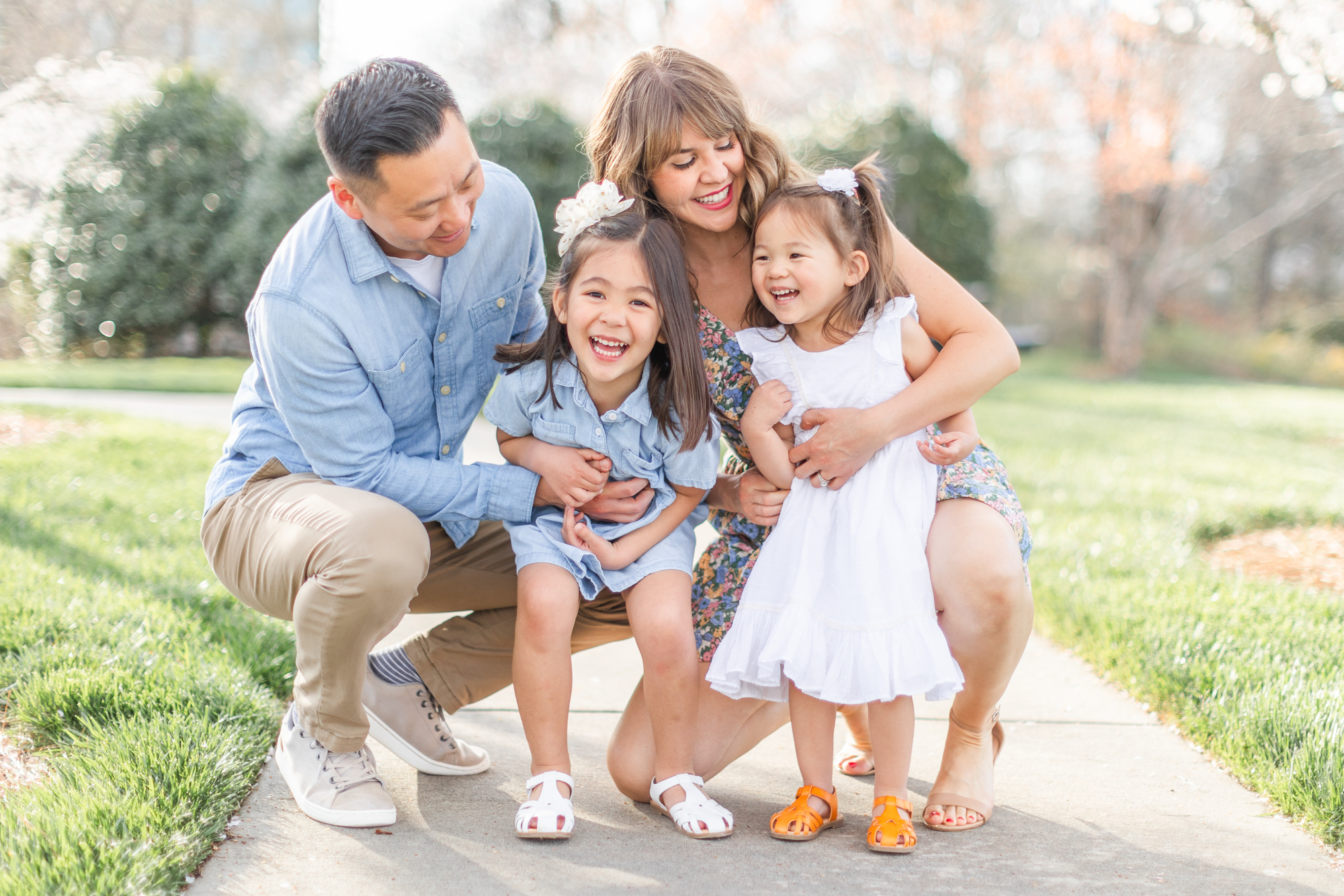 Charlotte Spring Minis. Family of four hugging and laughing together. 2 daughters standing and mom and dad are squatting behind them, coming in for a hug and tickles.